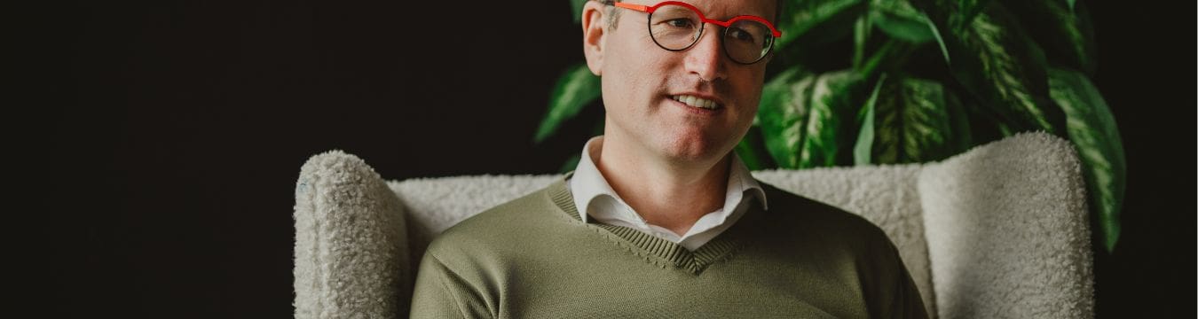 Simon Croonenbroeck - Über mich Simon Croonenbroeck sitzt entspannt in einem Sessel un blickt ruhig und ie Kamera